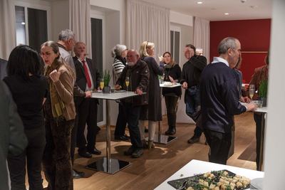 Empfang nach der Eröffnung: Gäste stehen mit Sekt und Häppchen an Stehtischen, vorne eine Platte mit Fingerfood.