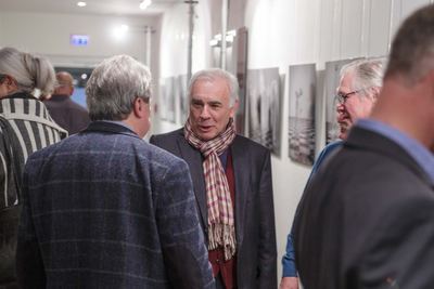 Gäste unterhalten sich in einem Flur, an dessen Wand eine Reihe von Schwarzweißfotografien mit Schachbrettmotiven hängt.