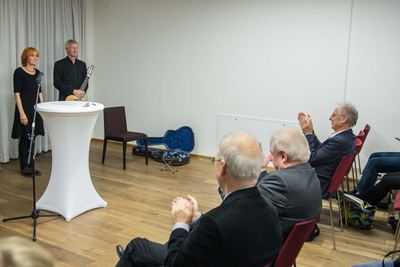 Die Vortragende und der Gitarrist nehmen lächelnd den Applaus des Publikums entgegen; daneben ein offener Gitarrenkoffer.