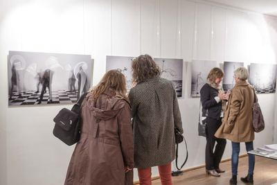 Besucherinnen betrachten Fotografien mit Lichtspuren und Wasserskulpturen über schwarzweiß karierten Böden.