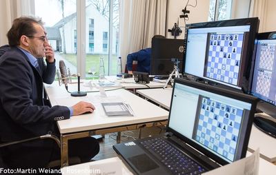 Kommentator am Mikrofon vor Monitoren und Laptop mit Schach960-Diagrammen für die Liveübertragung