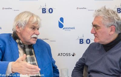 Gesprächsrunde im Übertragungsstudio vor einer Wand mit Sponsorenlogos, darunter B&O und ATOSS