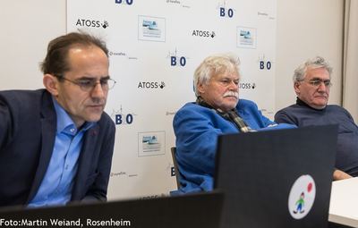 Drei Kommentatoren sitzen am Laptop vor der Sponsorenwand und verfolgen konzentriert die Partien