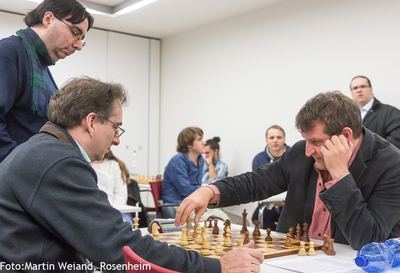 Spieler zieht eine Figur, sein Gegner stützt den Kopf in die Hand, ein Zuschauer schaut von der Seite zu