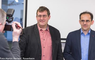 Zwei Männer stehen nebeneinander vor einer Leinwand und werden bei der Preisverleihung fotografiert
