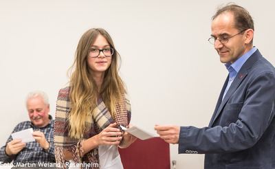 Junge Teilnehmerin mit Brille und Schal nimmt bei der Siegerehrung einen Umschlag entgegen