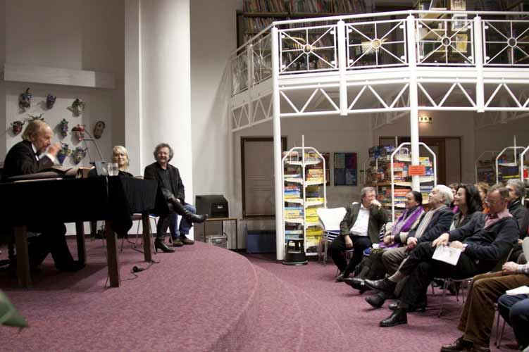 Diskussionsrunde nach der Aufführung: drei Personen auf der Bühne, gegenüber Zuschauer im Halbkreis vor Bücherregalen und Galerie