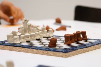 Selbstgemachtes Schachspiel: weiße und terrakottafarbene Tonfiguren auf einem Mosaikbrett mit blauem Rand
