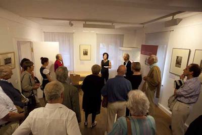 Führung durch die Ausstellung: Besucher stehen im Halbkreis um eine Frau, an den Wänden gerahmte Grafiken