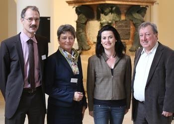 Vier Personen stehen nebeneinander für ein Gruppenbild vor einem Brunnendenkmal im Museumssaal