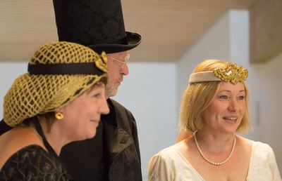 Kostümierte Figuren vor der Partie: schwarze Dame mit goldenem Haarnetz, Mann mit Zylinder und weiße Dame mit Diadem