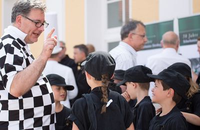 Mann im schwarz-weiß karierten Trikot gibt den als schwarze Bauern gekleideten Kindern letzte Anweisungen