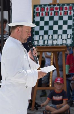 Weißer Turm mit hohem weißem Hut spricht das Grußwort ins Mikrofon, hinter ihm das Demonstrationsbrett und sitzende Kinder