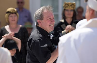 Lachender Moderator mit Mikrofon zwischen den kostümierten Figuren, hinten die schwarze Dame und der schwarze König