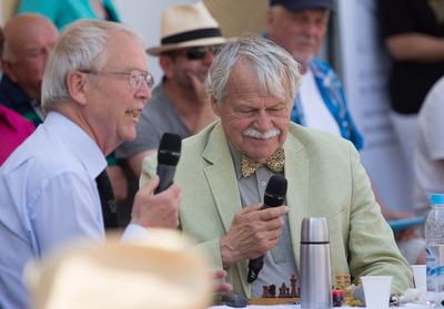 Die beiden kommentierenden Großmeister mit Mikrofonen am Tisch, vor ihnen ein kleines Schachbrett und eine Thermoskanne