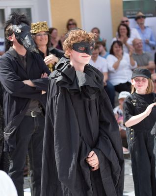 Schwarzer Bauer mit Augenmaske und weitem schwarzem Umhang, hinter ihm ein schwarzer Springer und applaudierende Zuschauer