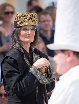 Schwarzer König mit verzierter Goldkrone stützt sich auf sein Zepter, rechts angeschnitten ein weißer Turm