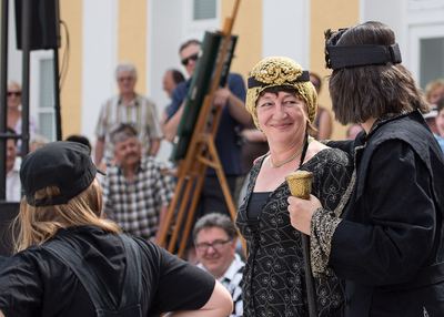Schwarze Dame und schwarzer König mit Zepter im Gespräch auf dem Spielfeld, dahinter Zuschauer und das Demonstrationsbrett