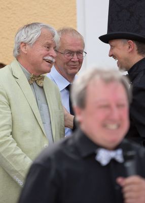 Die beiden Großmeister lachen mit einem schwarzen Läufer, vorn unscharf der Moderator mit Fliege
