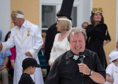 Lachender Moderator mit Mikrofon, hinter ihm die Königspaare beider Farben und ein schwarzer Läufer