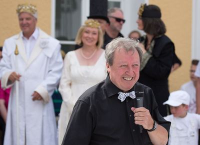 Moderator mit Fliege und Mikrofon, im Hintergrund weißer König mit Zepter, weiße Dame und schwarze Figuren
