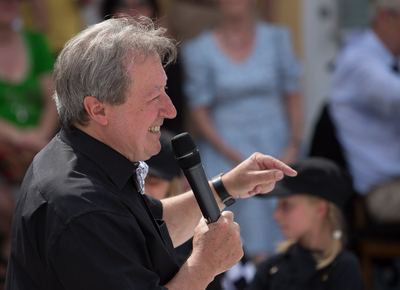 Moderator im schwarzen Hemd zeigt lachend mit dem Finger ins Publikum, das Mikrofon in der Hand