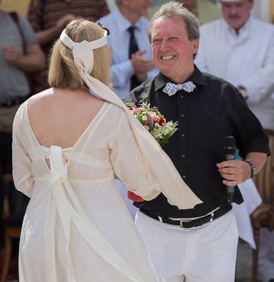 Moderator überreicht der weißen Dame im langen cremefarbenen Kleid einen bunten Blumenstrauß