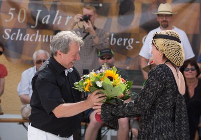 Die schwarze Dame erhält einen Sonnenblumenstrauß, dahinter ein Banner „50 Jahre Schachunion“