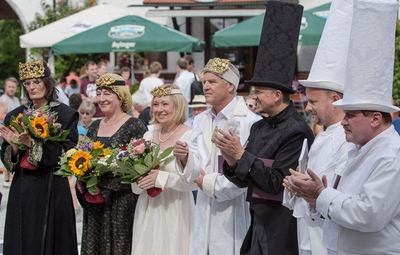 Die Hauptfiguren beider Farben aufgereiht mit Blumen und Urkunden, applaudierend vor Biergarten-Schirmen