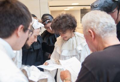 Kostümierte Mitspieler mit Halskrausen und Masken studieren vor dem Auftritt den Zugablauf auf Papierbögen