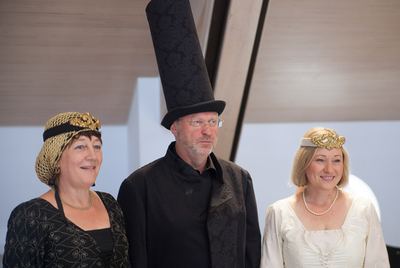 Schwarze Dame, schwarzer Läufer mit hohem Brokathut und weiße Dame mit Diadem posieren nebeneinander im Saal