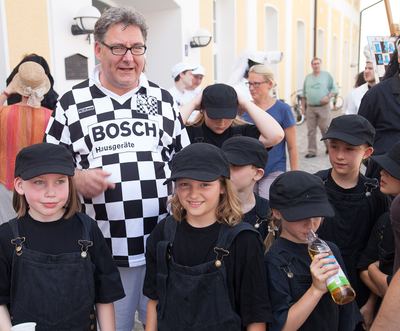 Mann im karierten Trikot mit Kindern in schwarzen Latzhosen und Kappen, den schwarzen Bauern