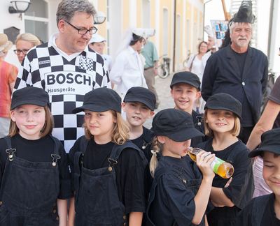 Gruppenbild der schwarzen Bauern in Latzhosen und Kappen, hinten ein Betreuer im Karotrikot und ein schwarzer Springer