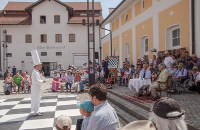 Grußwort des weißen Turms am Feldrand, rechts der Kommentatorentisch, hinten die Alte Brennerei und Zuschauer