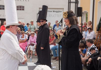 Der schwarze König auf sein Zepter gestützt gegenüber einem lachenden weißen Turm, dahinter ein schwarzer Läufer