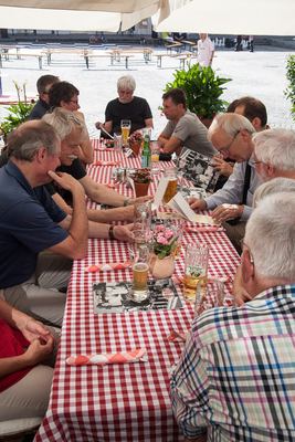 Geselliges Beisammensein an einer langen Tafel mit rot-weiß karierter Decke, Bierkrügen und Fotos