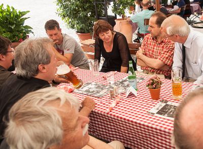 Gesprächsrunde am rot-weiß karierten Tisch mit Weißbier, Mineralwasser und Schwarz-Weiß-Fotos als Tischsets
