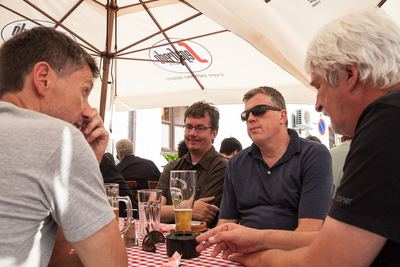Vier Männer unterhalten sich unter einem Sonnenschirm bei Bier am karierten Tisch