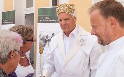 Weißer König mit Zepter im Gespräch mit Besucherinnen vor Ausstellungstafeln „50 Jahre Schachunion Ebersberg-Grafing“