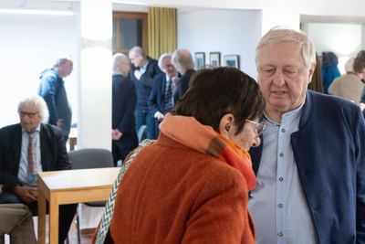 Gäste der Ausstellungseröffnung im Gespräch in den Räumen der Stadtbücherei Grafing, vorn eine Frau in orangem Mantel