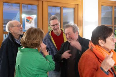 Gruppe von Gästen unterhält sich lachend vor der verglasten Holztür der Stadtbücherei mit Ausgangsschild
