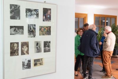 Gerahmte Tafel mit alten Filmfotos und Autogrammkarten von Schachszenen, dahinter unscharf plaudernde Gäste