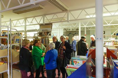 Gäste stehen plaudernd zwischen Kinderbuchregalen und Bücherständern in der hellen Halle der Stadtbücherei Grafing