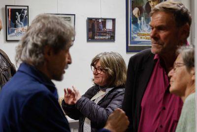 Lebhaftes Gespräch unter Gästen vor gerahmten Filmplakaten, darunter „Bauernopfer“ und „L’Échiquier de la passion“