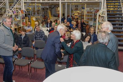 Herzliche Begrüßung zwischen den Stuhlreihen, während das Publikum vor Treppe und Bücherregalen Platz nimmt