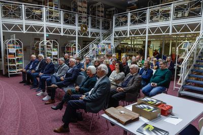 Voll besetzte Stuhlreihen unter den weißen Galerien der Bücherei, vorn ein Tisch mit Katalogkartons „Schach und Film“ und roter Kasse
