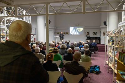 Volle Stuhlreihen zwischen Bücherregalen der Stadtbücherei Grafing, vorn spricht der Redner vor der Projektion „Schach und Film“