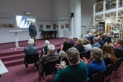Beifall des Publikums für den Redner auf der Bühne, hinter ihm die Leinwand „Schach und Film“ und gerahmte Filmplakate