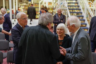 Nach den Reden: kleine Gesprächsrunde zwischen den Stuhlreihen, ein Herr im grauen Anzug gestikuliert, dahinter die blaue Treppe