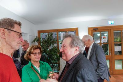 Gäste mit Sektglas im Foyer der Bücherei vor holzgerahmten Glastüren und einer großen Zimmerpflanze